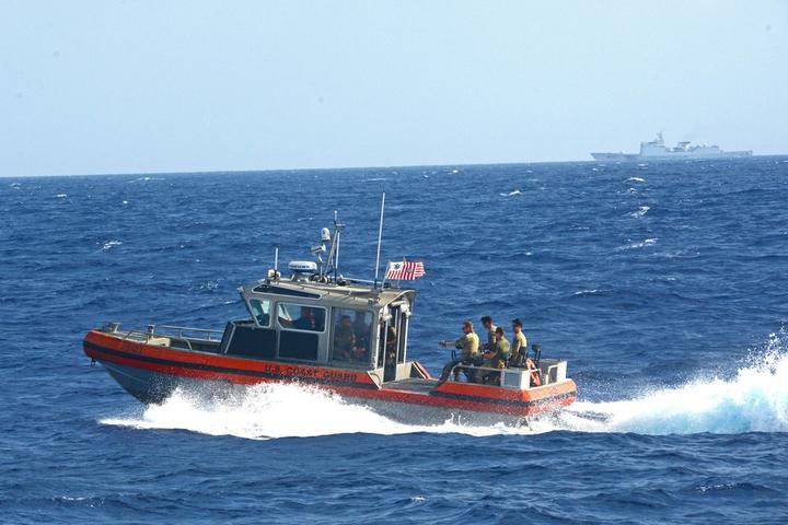 A U.S. Coast Guard small boat moves across the South China Sea with a China Coast Guard vessel visible on the horizon.