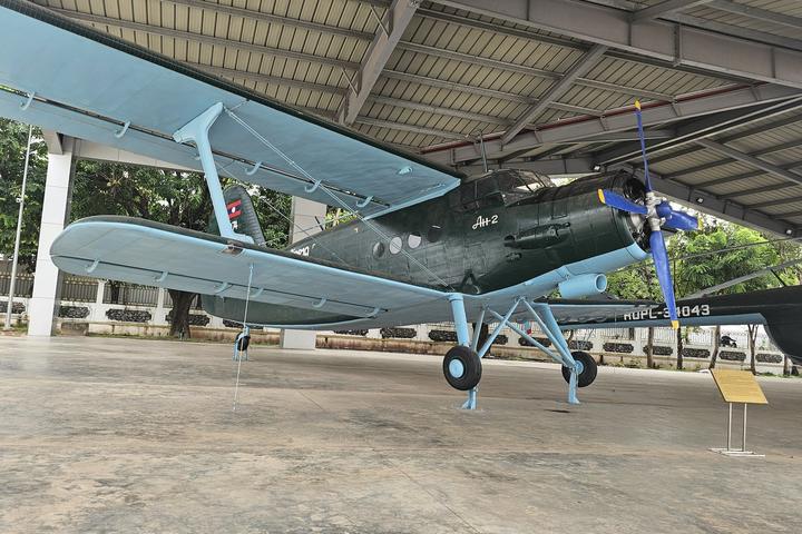 A preserved olive-green propeller aircraft displayed under a roof at the Lao People's Army Historical Museum in Vientiane, Laos.