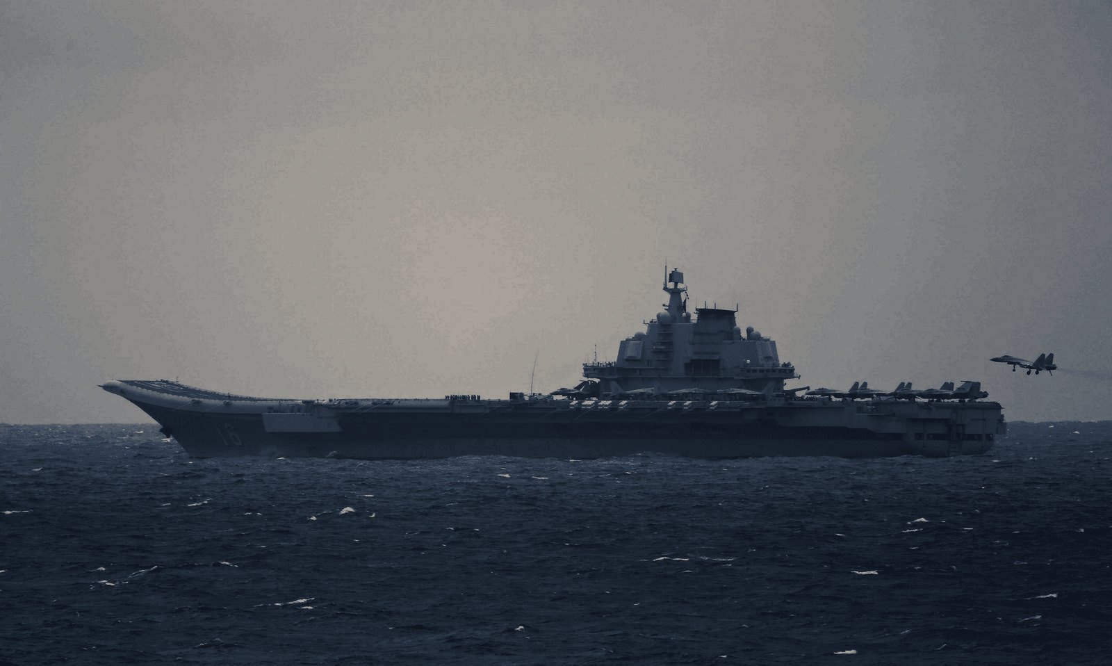 A J-15 carrier-based fighter on final approach to the aircraft carrier Liaoning, landing gear and arresting hook down, seen from astern